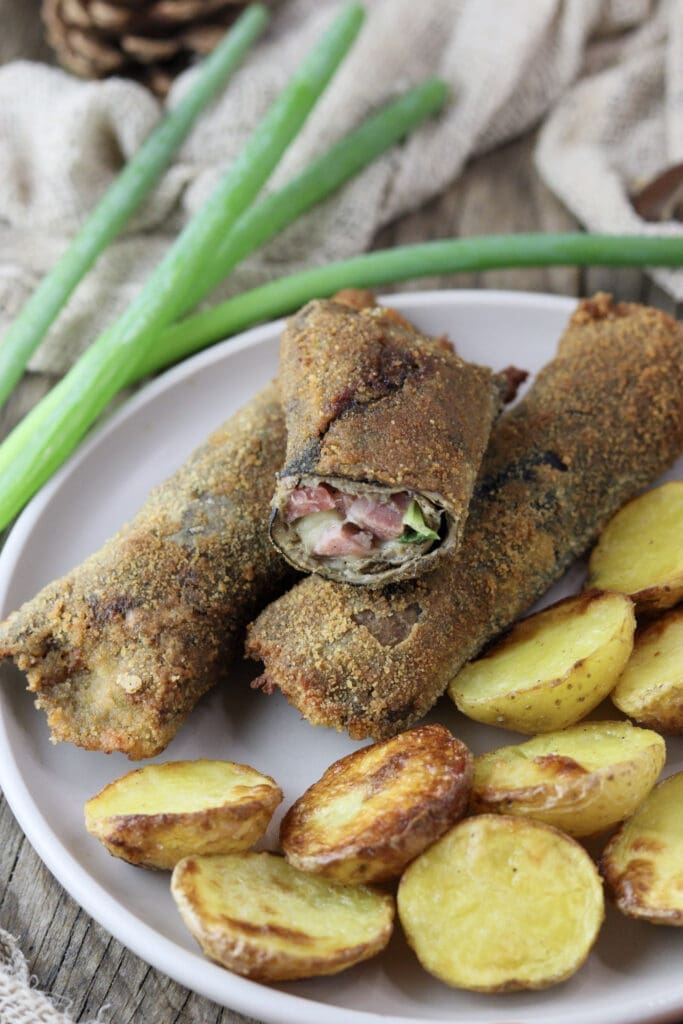 breaded fried parasol mushroom rolls filled with bacon, young onion and cheese on a wooden table with a pine cone in the background
